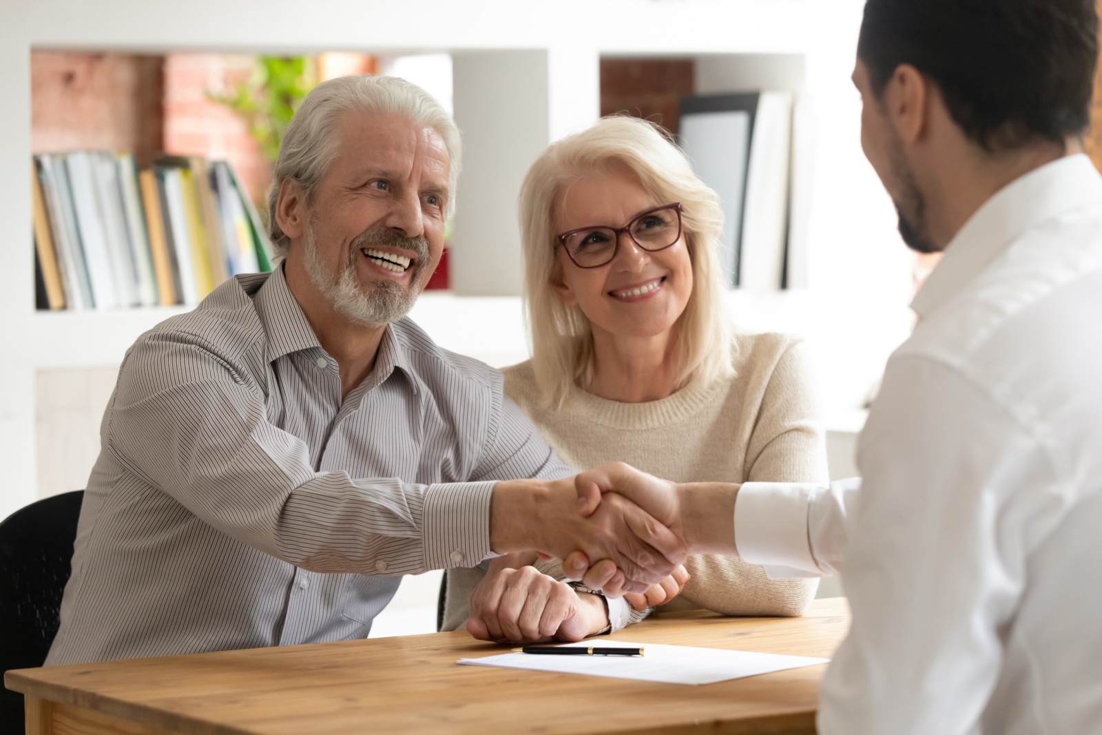 Happy senior old family couple clients make financial insurance estate business deal handshake agent lawyer, satisfied mature customers shake hand meeting bank manager agree on investment contract