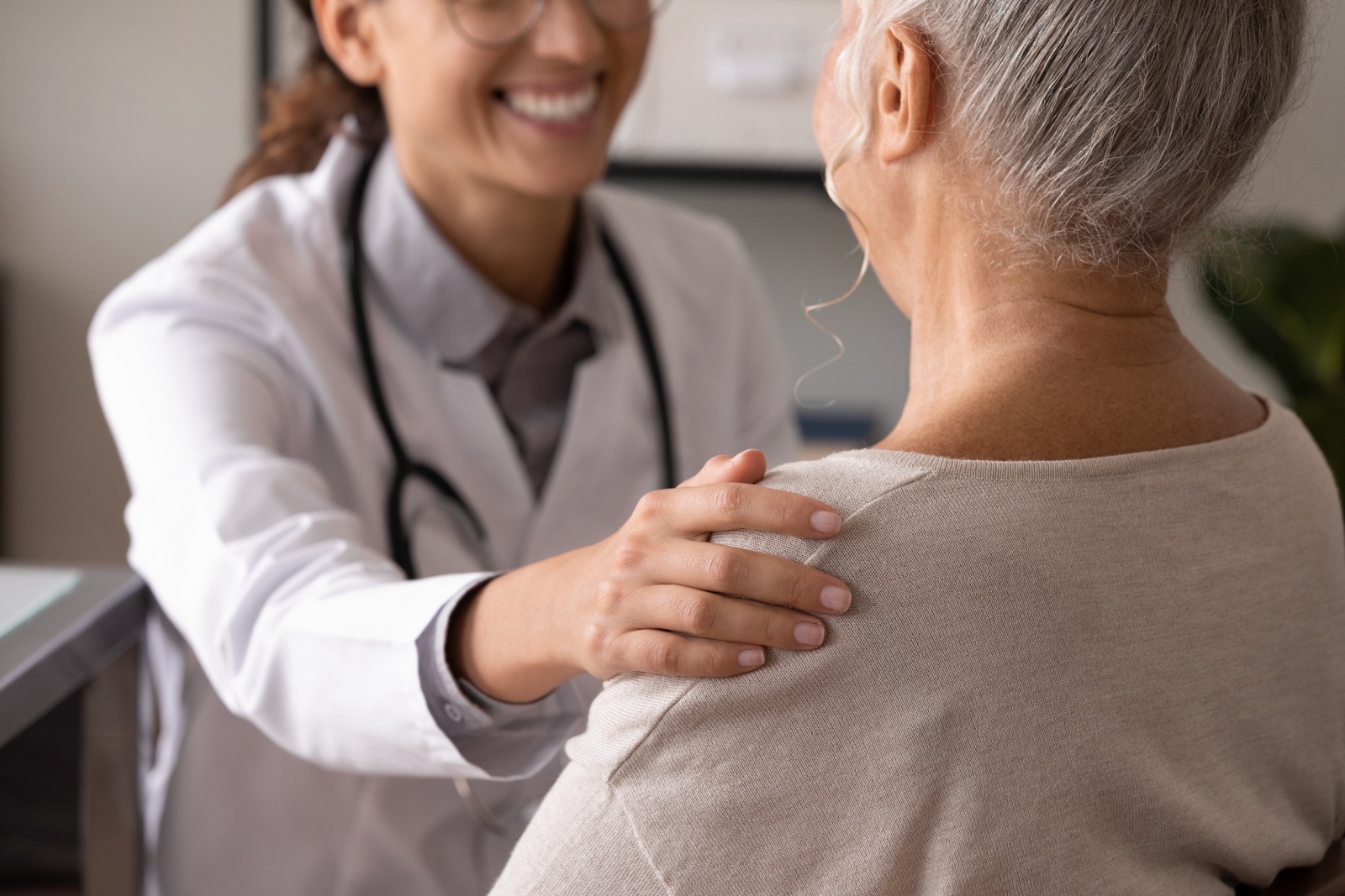 Close up back view smiling female doctor wearing uniform touching mature patient shoulder, expressing empathy and care, successful treatment or medical checkup result, psychological help concept