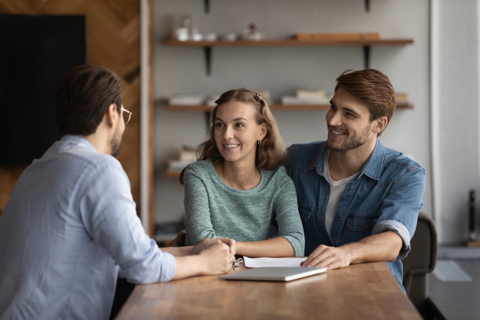Happy young married family couple consulting Real Estate Agent, agent, advisor, consultant, talking on meeting, discussing real estate property buying, mortgage, house rent, smiling, laughing